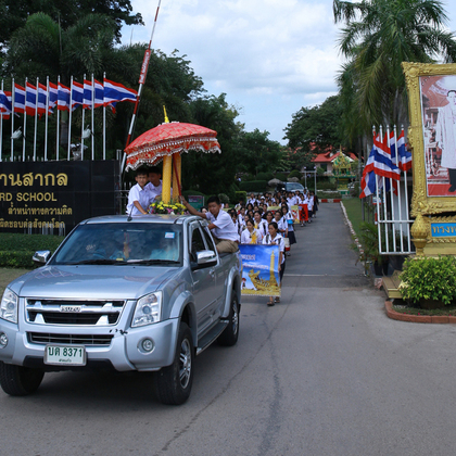 Die Parade zum Tempel zum Beginn der Regenzeit. Außerdem sieht man den aufwendig gestalteten Eingang zum Schulgelände, mit einem der unzähligen Bildern des thailändischen Königs.